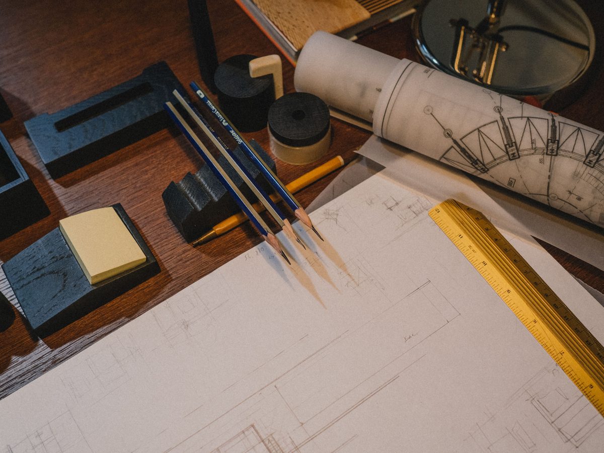 Architectural drawing on a drafting desk with pencils, a scale ruler and a rolled technical drawing